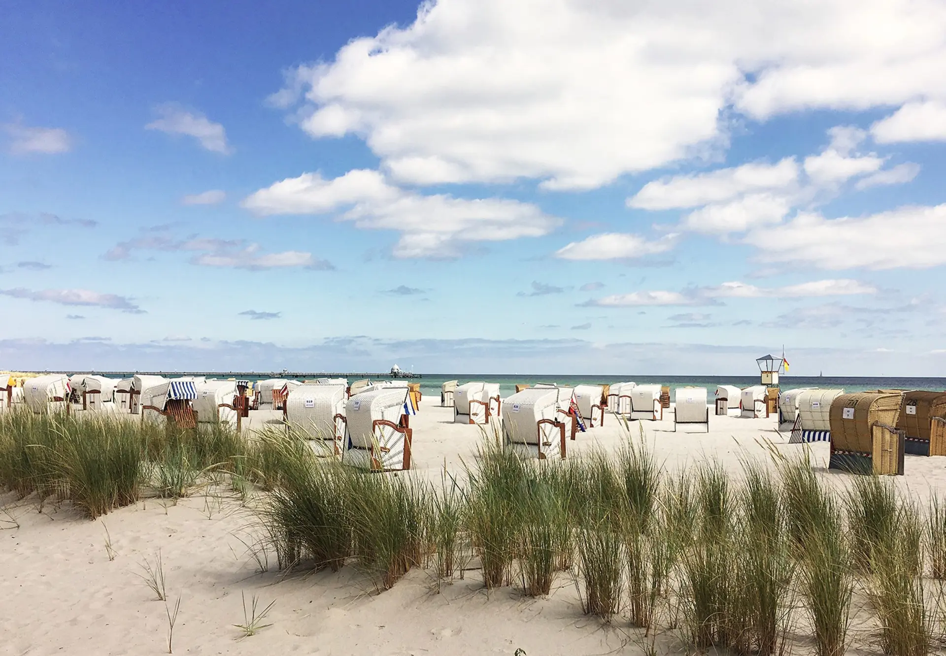 Viele Strandkörbe stehen auf einem Sandstrand vor einem blauen Himmel.