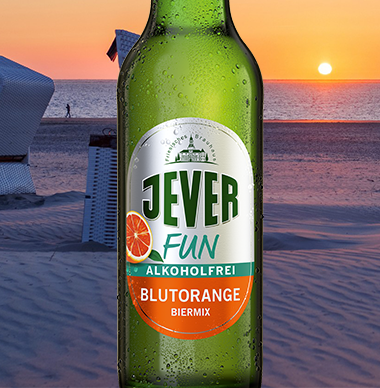 Eine grüne Flasche steht im Vordergrund vor einem Strand bei Sonnenuntergang.