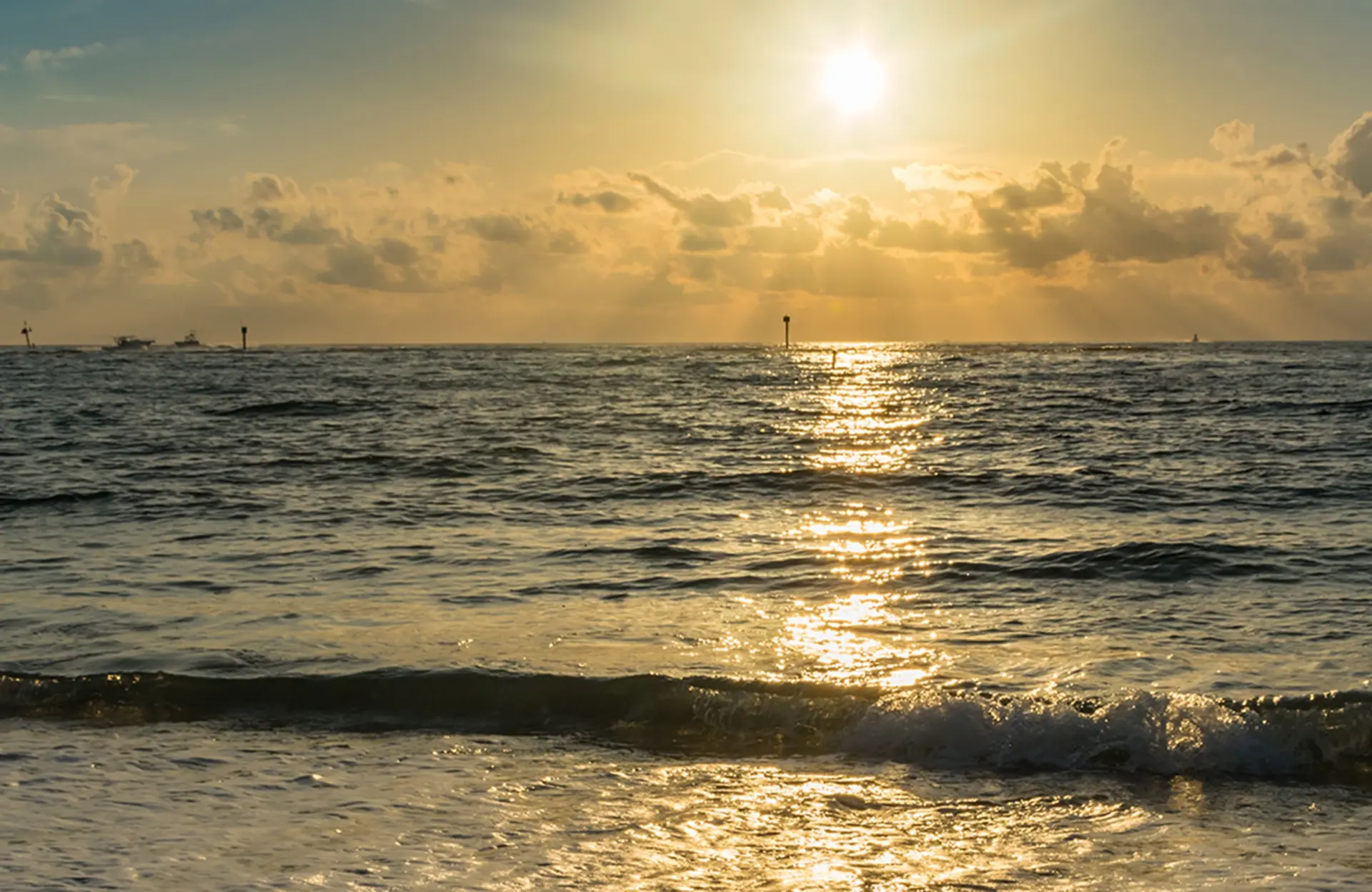 Sonnenuntergang spiegelt sich auf dem welligen Meer, leichte Wolken am Himmel.