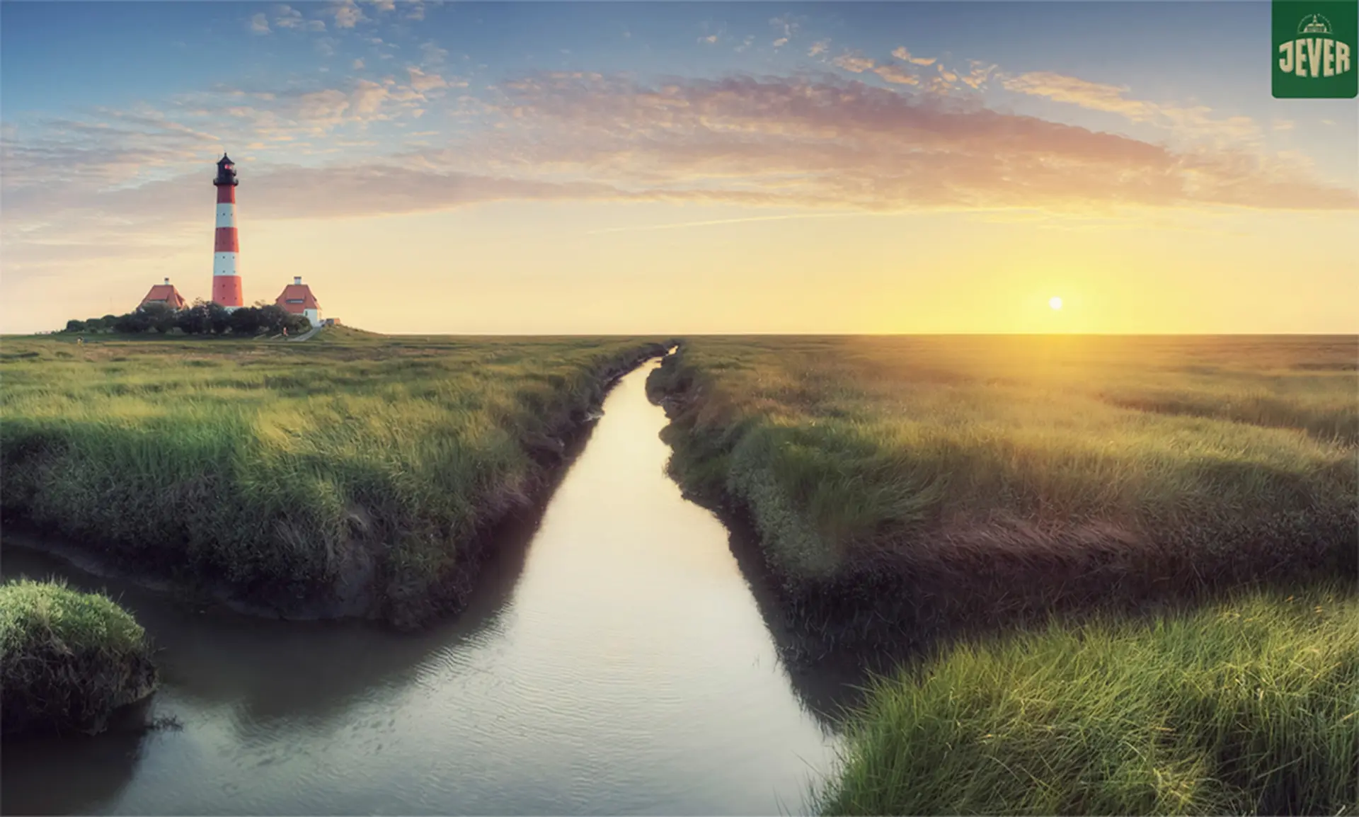 Ein Leuchtturm steht in einer Marschlandschaft bei Sonnenuntergang, umgeben von grünem Gras und einem Wasserlauf.