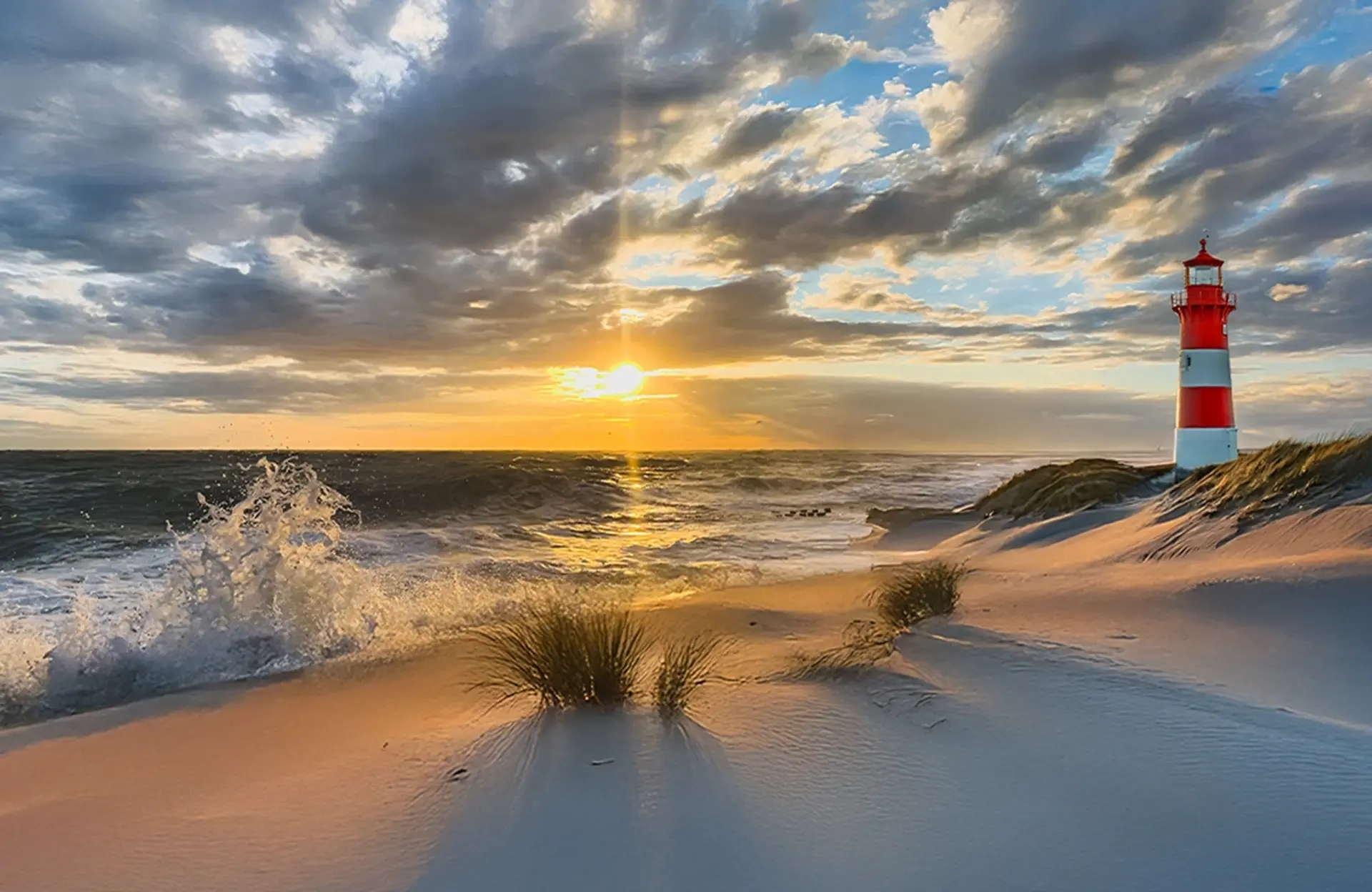 Ein rot-weiß gestreifter Leuchtturm steht am aufgewühlten Meer bei Sonnenuntergang.