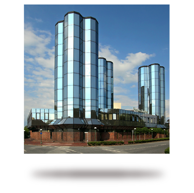 Moderne Glasgebäude mit drei Türmen unter blauem Himmel stehen neben einem traditionellen Backsteinbau.