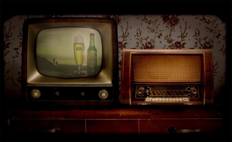 Ein alter Fernseher zeigt ein Bierglas und eine Flasche, neben ihm steht ein Retro-Radiogerät.