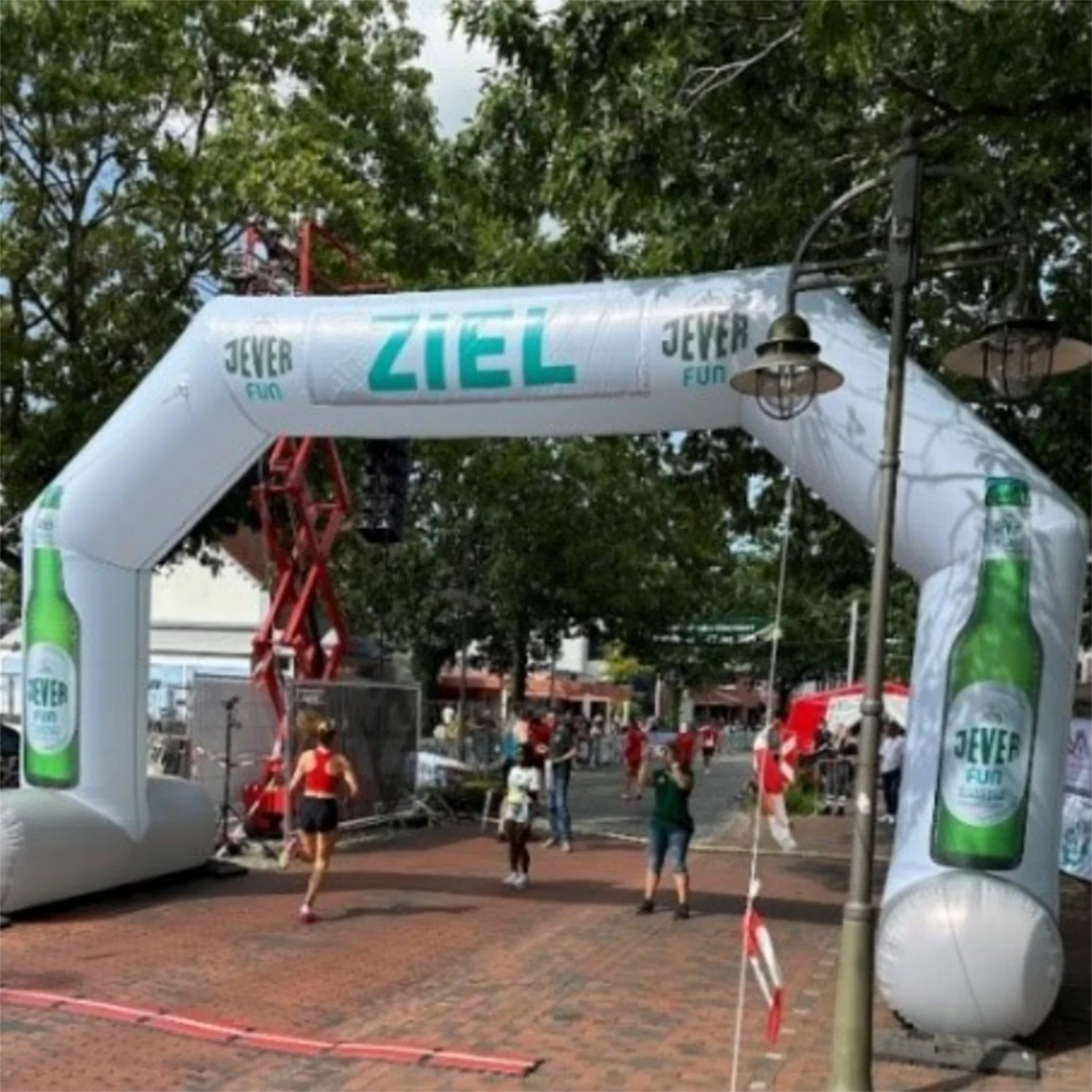 Läuferin überquert eine Zielmarke aus weißem Jever-Fun-Bogen. Weitere Teilnehmer und Zuschauer im Start-Ziel-Bereich.