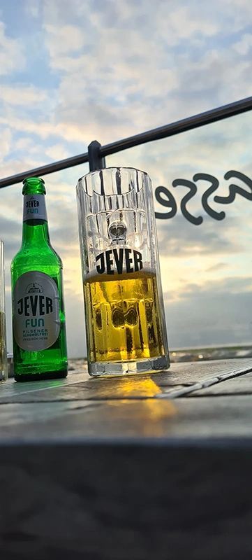 Ein Glas mit hellem Getränk steht auf einem Holztisch, dahinter eine grüne Flasche.