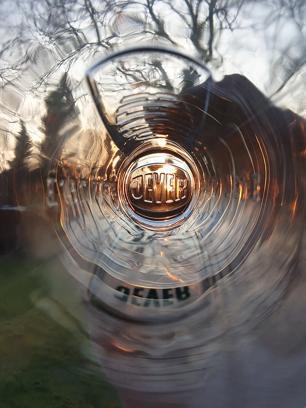 Ein verschwommenes Glas mit Lichtreflexionen steht vor einem Hintergrund aus Bäumen.