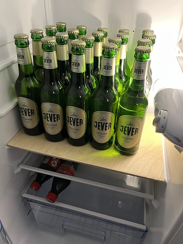 Mehrere grüne Bierflaschen stehen auf einem Holzbrett in einem Kühlschrank.