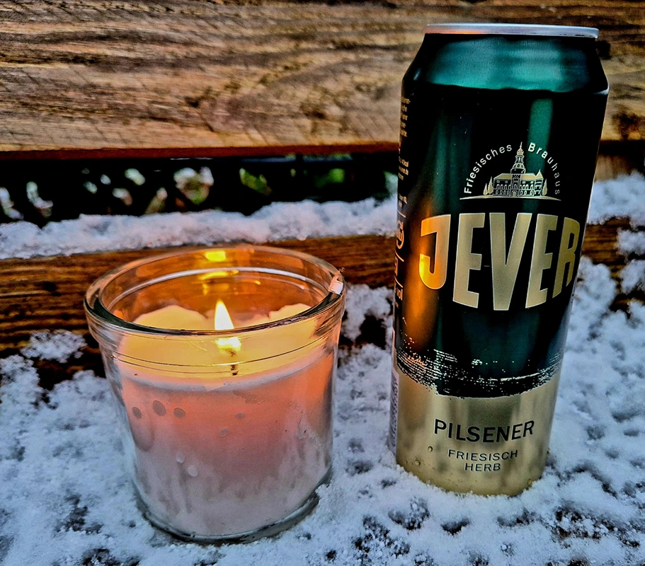 Eine Getränkedose steht neben einer brennenden Kerze im Schnee auf Holz.