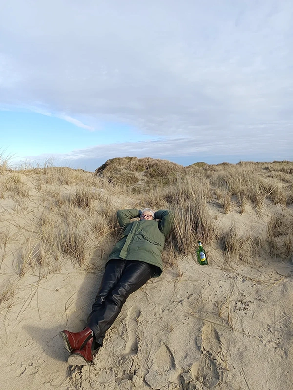 Eine Person liegt entspannt auf dem Sand in einer Dünenlandschaft mit einer Flasche neben sich.
