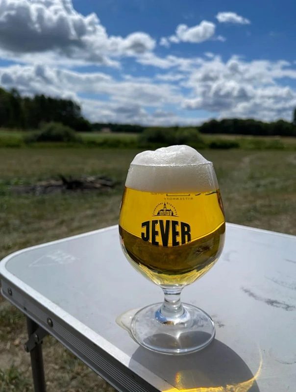Ein Bierglas steht auf einem Tisch im Freien, mit Wiesen und bewölktem Himmel im Hintergrund.