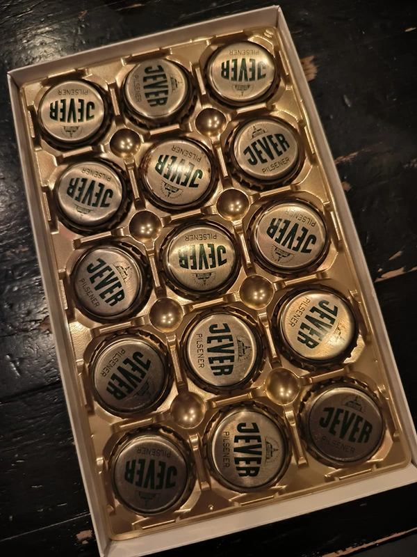 Eine Packung mit mehreren goldfarbenen Flaschendeckeln in einem weißen Tablett.