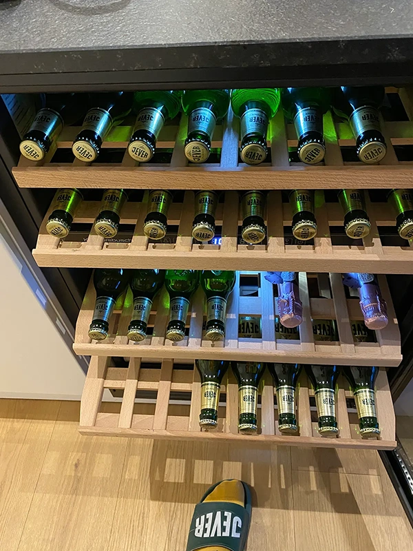 Grüne Glasflaschen liegen auf einem Holzregal, darunter steht eine Sandale.