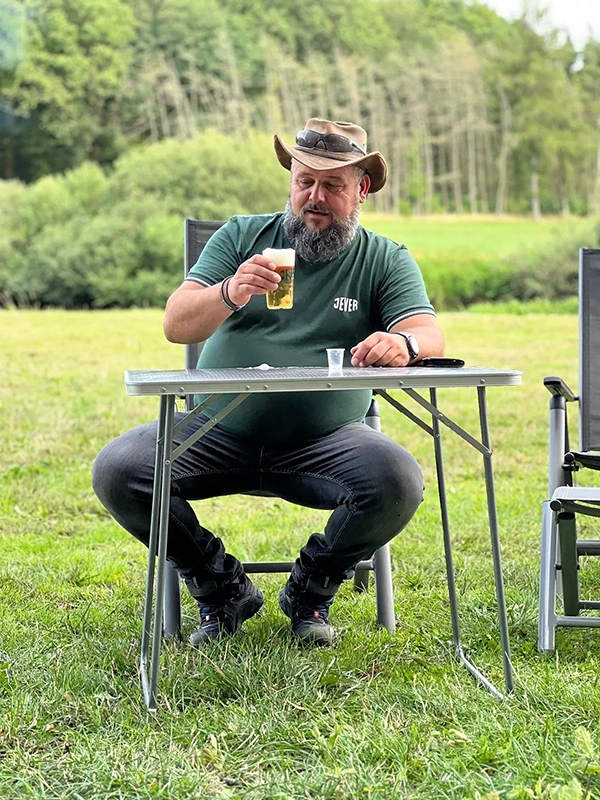 Ein Mann mit Hut sitzt im Freien und trinkt aus einem Bierglas.
