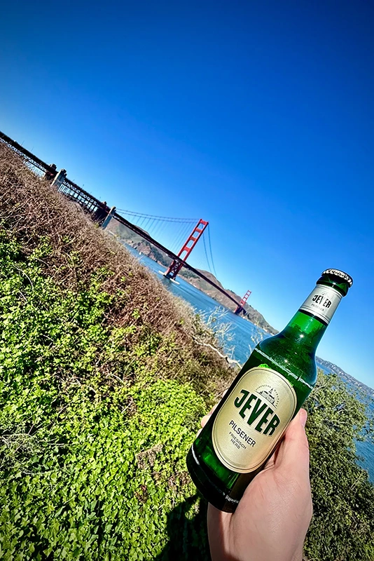 Eine Hand hält ein Bier mit einer berühmten roten Brücke im Hintergrund.
