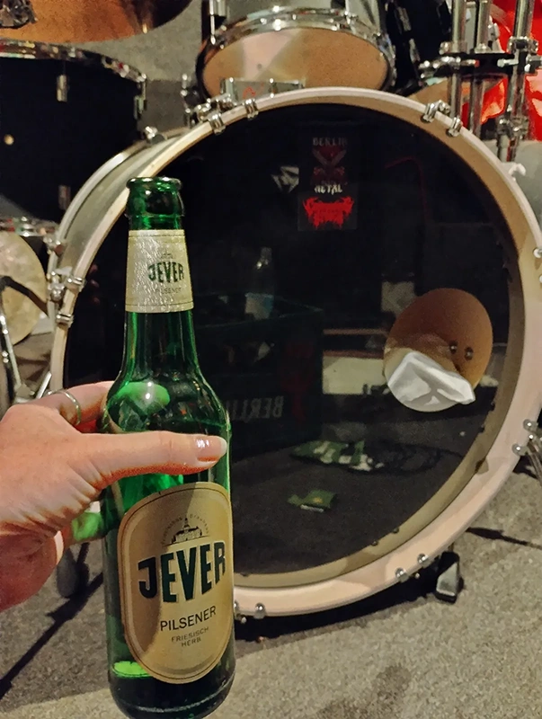 Eine Hand hält eine grüne Bierflasche vor einer Bassdrum.