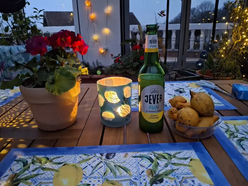 Ein Tisch bei Abenddämmerung ist mit einer Flasche, einer Kerze, einer Blumenpflanze und Birnen dekoriert.