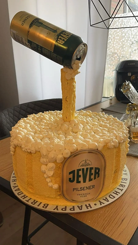 Eine Torte ist kreativ gestaltet als Bierkrug mit fließend aussehendem Schaum aus kleinen weißen Kugeln.