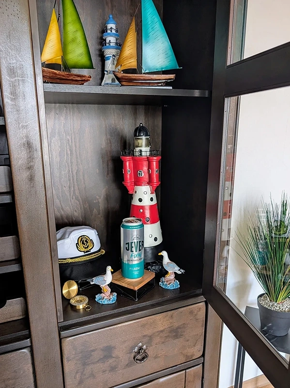 Ein Regal ist gefüllt mit maritimen Dekorationsobjekten, darunter Modelle von Schiffen und ein Leuchtturm.