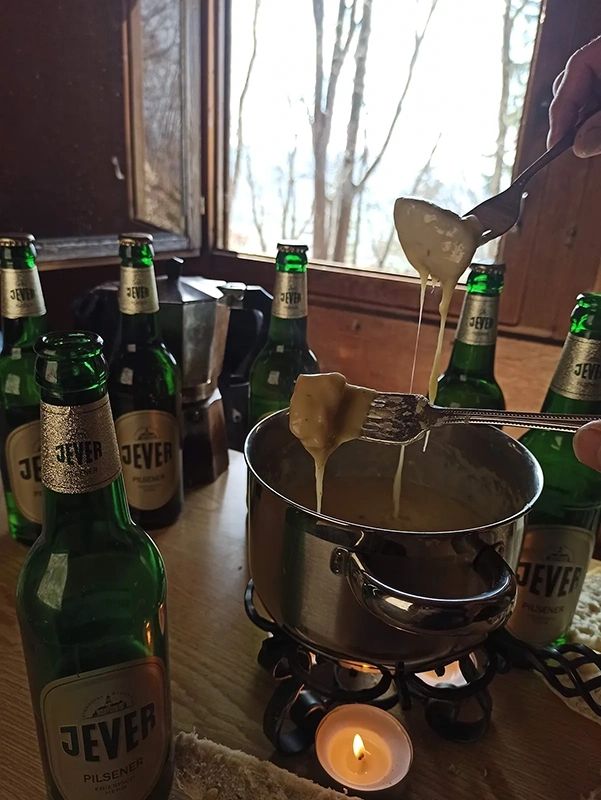 Eine Person schöpft mit einem Löffel geschmolzenen Käse aus einem Fondue-Topf.