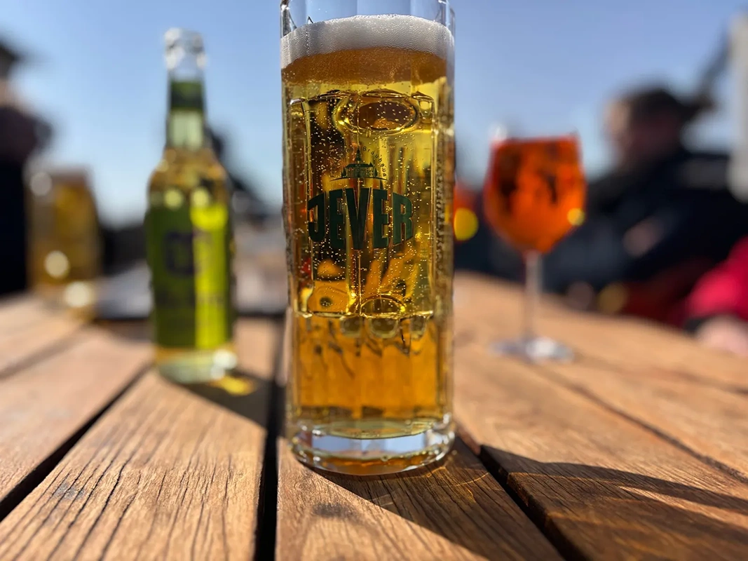 Ein Glas Bier und eine Flasche stehen scharf im Vordergrund auf einem Holztisch.