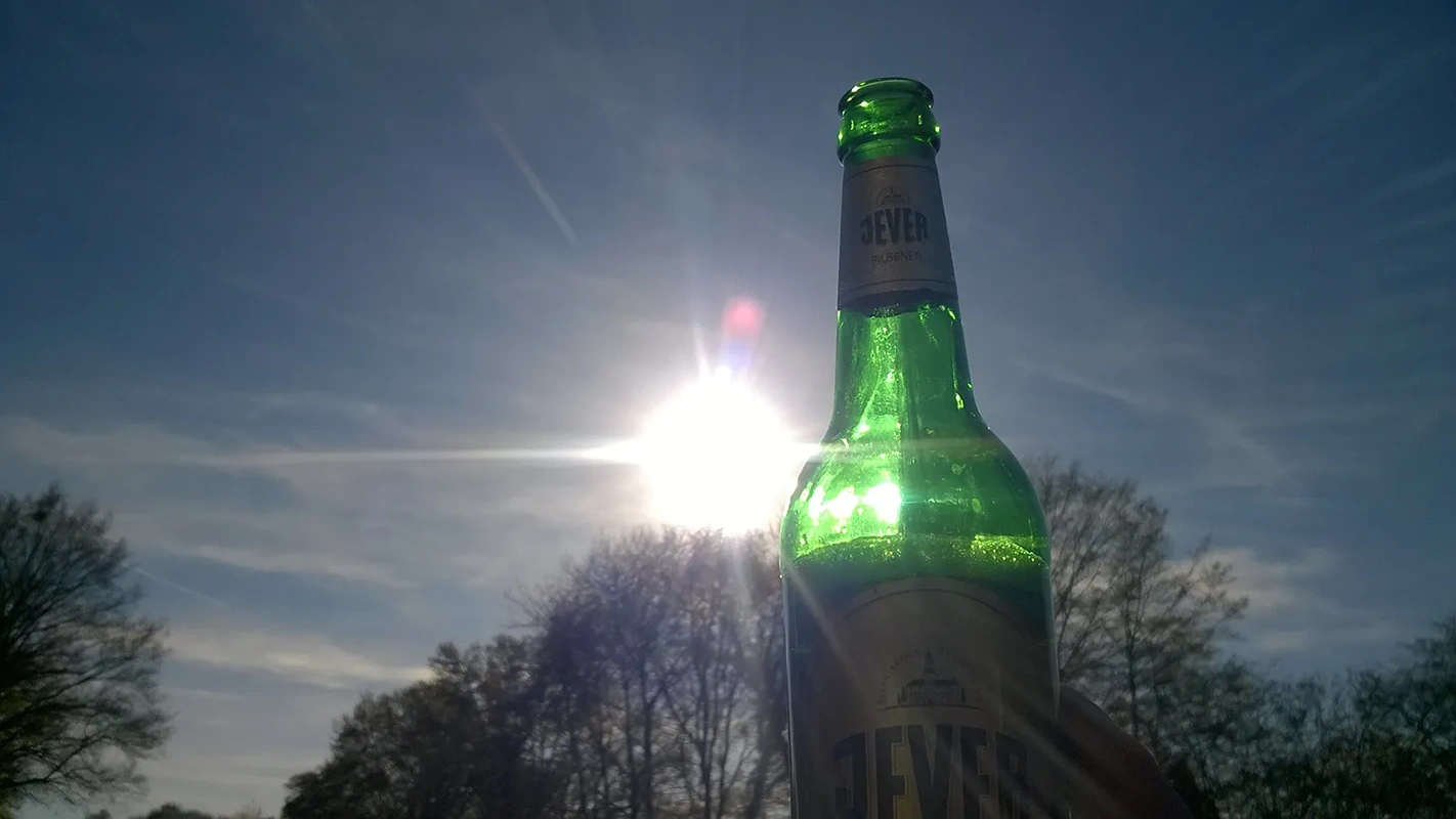 Eine grüne Glasflasche wird vor der Sonne gehalten und erzeugt eine Lichtreflexion.