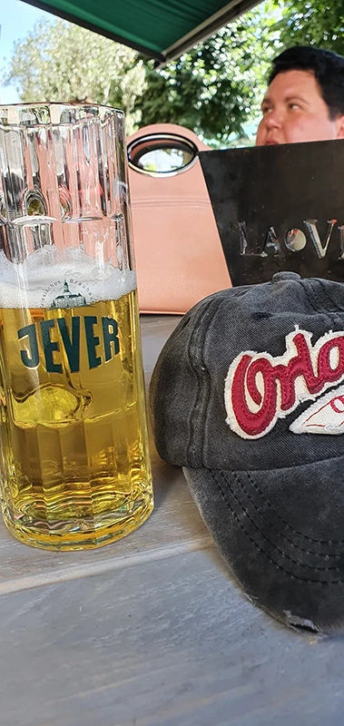 Ein Bierglas steht neben einer abgelegten Kappe auf einem Tisch im Freien.
