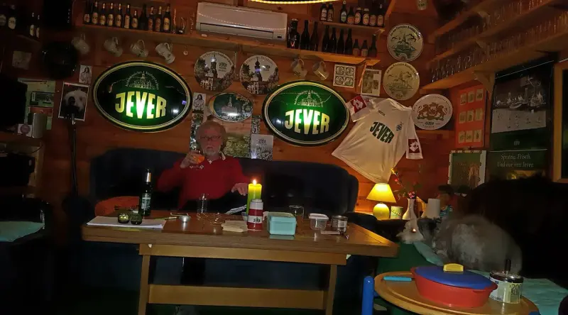 Eine Person sitzt an einem Tisch in einem gemütlichen Raum mit einer Katze neben sich.