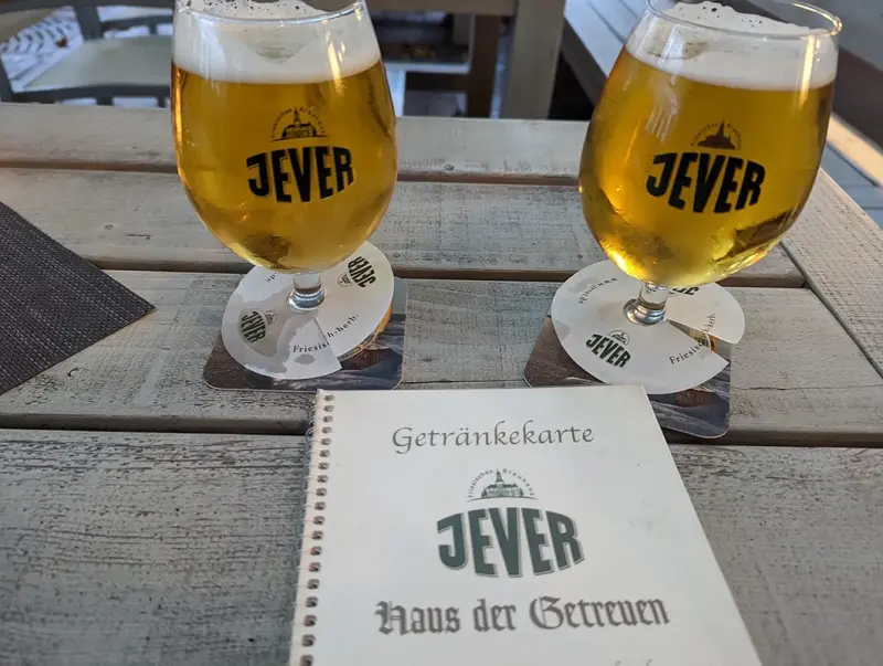 Zwei Gläser mit hellem Bier stehen auf einem Holztisch neben einer Getränkekarte.