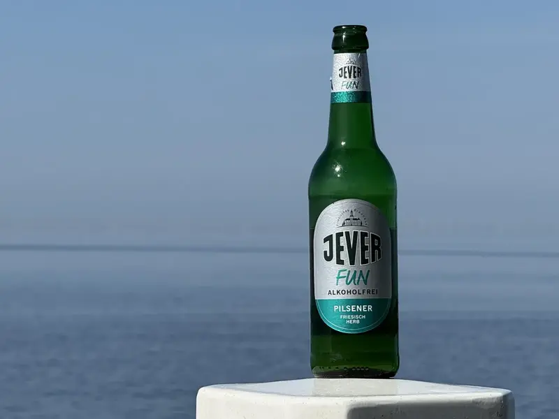 Eine grüne Flasche steht auf einem weißen Pfosten vor einem ruhigen Meer.