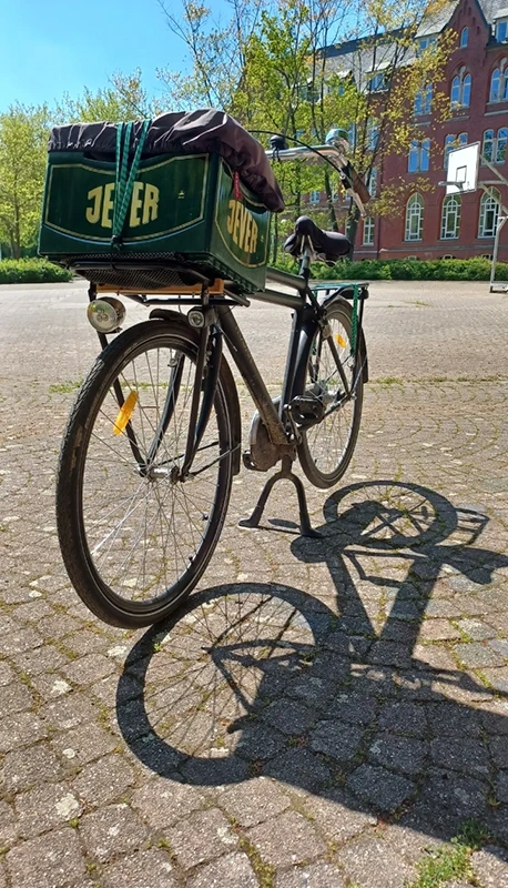 Ein schwarzes Lastenfahrrad steht auf einem gepflasterten Platz vor einem roten Backsteingebäude.