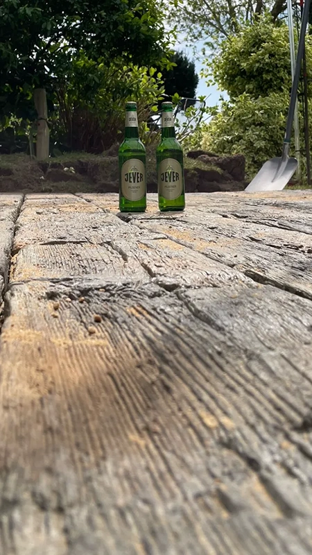 Zwei grüne Bierflaschen stehen auf einem alten Holztisch im Garten.