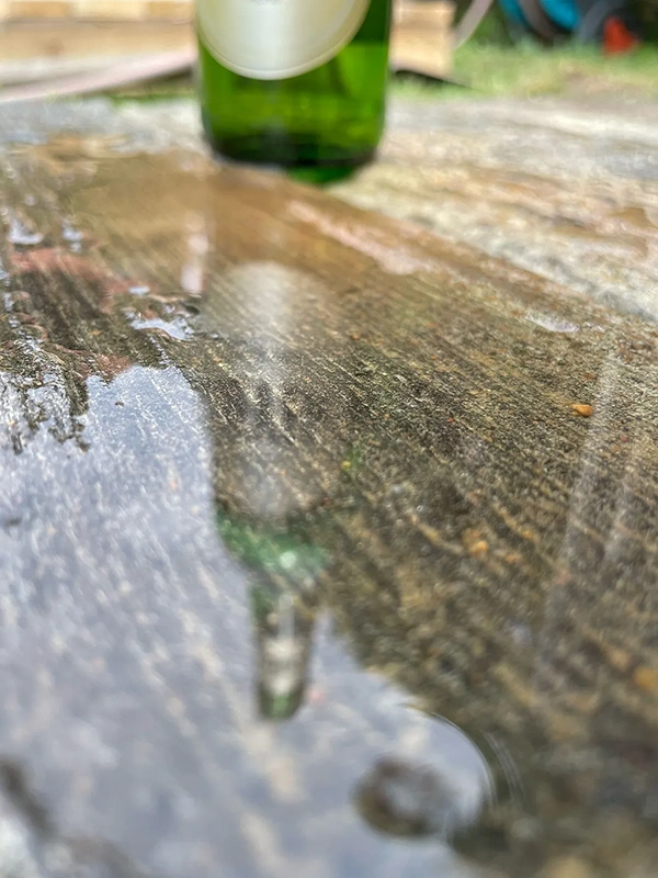 Eine grüne Flasche steht auf einer nassen Holzoberfläche, im Hintergrund unscharf.
