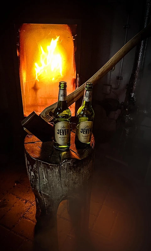 Zwei Flaschen Bier stehen auf einem Holzblock vor einem lodernden Kaminfeuer.