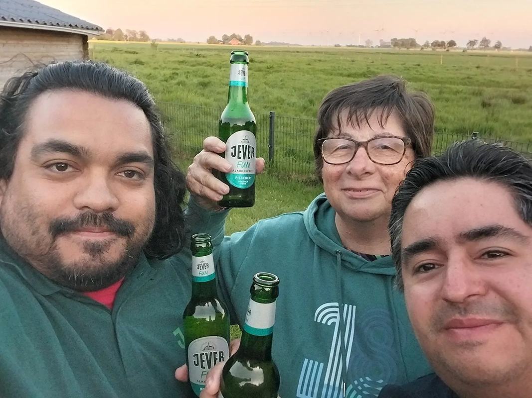 Drei Personen lächeln mit Getränkeflaschen in der Hand vor einer Wiesenlandschaft.