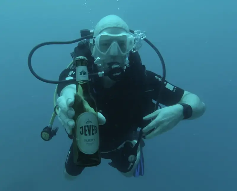 Ein Taucher unter Wasser hält eine Flasche in der Hand und atmet durch einen Atemregler.