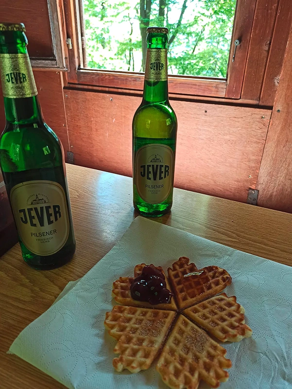 Zwei grüne Bierflaschen stehen neben einem Waffelherz mit Marmelade auf einem Tisch.