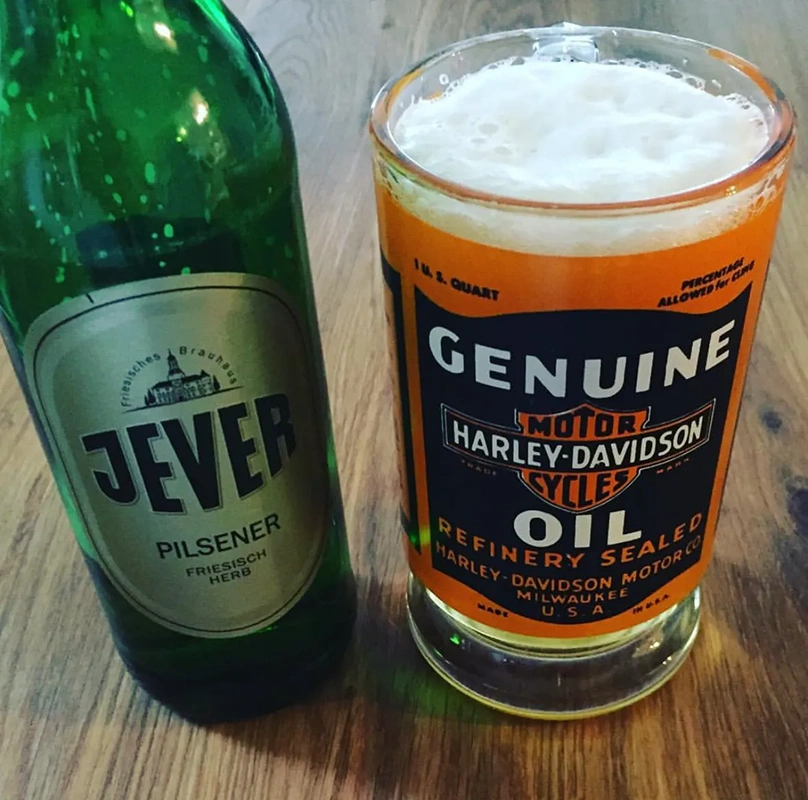 Ein grünes Bierflasche steht neben einem Glas mit Bierschaum auf einem Holztisch.