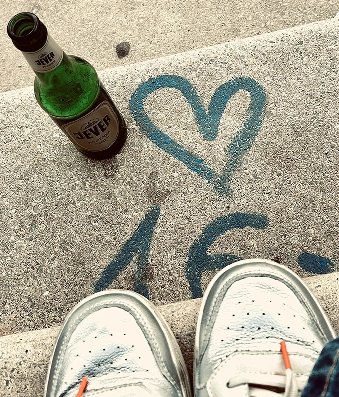 Jever Pilsener Flasche auf Betonstufe neben blauem Herz und Zahlen als Graffiti. Im Vordergrund silberne Turnschuhe.
