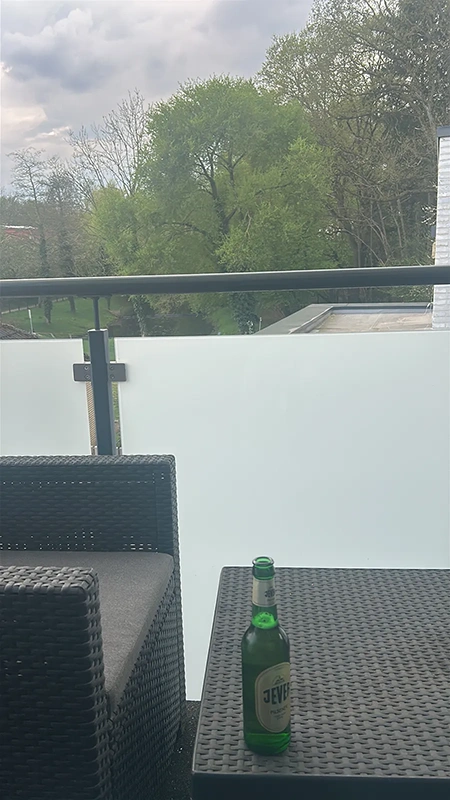 Eine Jever Pilsener Flasche steht auf einem Rattantisch.  Im Hintergrund Laubbäume und ein bewölkter Himmel.