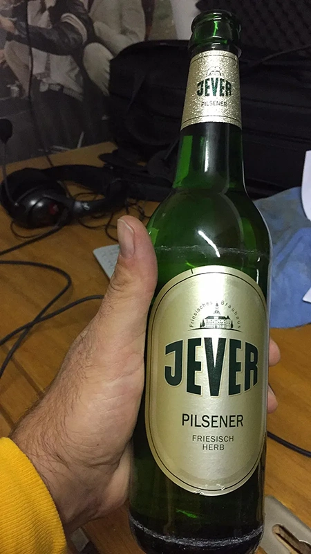 Jever Pilsener Flasche wird von einer Hand gehalten. Im Hintergrund ein Schreibtisch mit Technik.