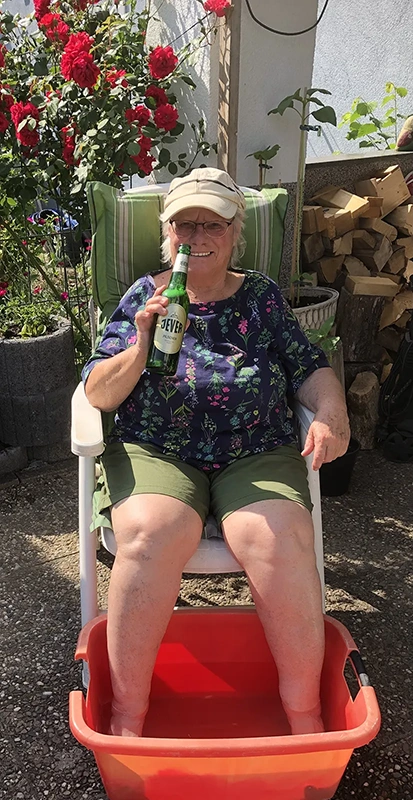 Frau sitzt auf einem Gartenstuhl mit Jever Flasche in der Hand und Füßen in einer Wanne mit Wasser.