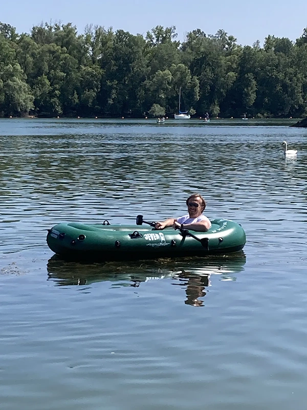 Mann sitzt in einem Jever Schlauchboot auf ruhigem Wasser. Im Hintergrund Bäume, ein Segelboot und ein Schwan.