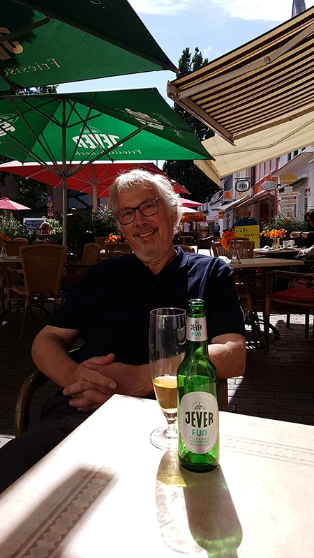 Ein älterer Mann sitzt an einem Tisch im Straßencafé, vor ihm ein Bierglas und eine Jever Flasche.