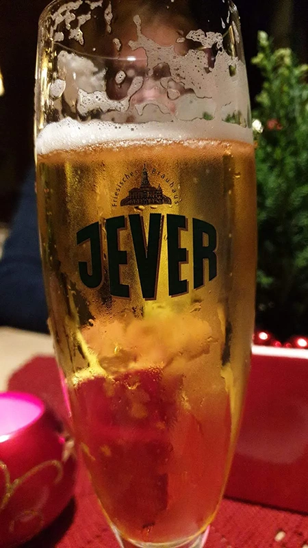 Ein hohes Glas mit goldfarbenem Bier und Jever Schriftzug steht auf einem roten Untersetzer.