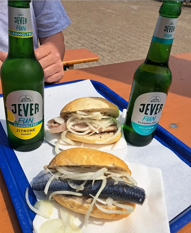 Zwei Fischbrötchen mit Zwiebeln und zwei Flaschen Jever Fun auf einem Tablett.