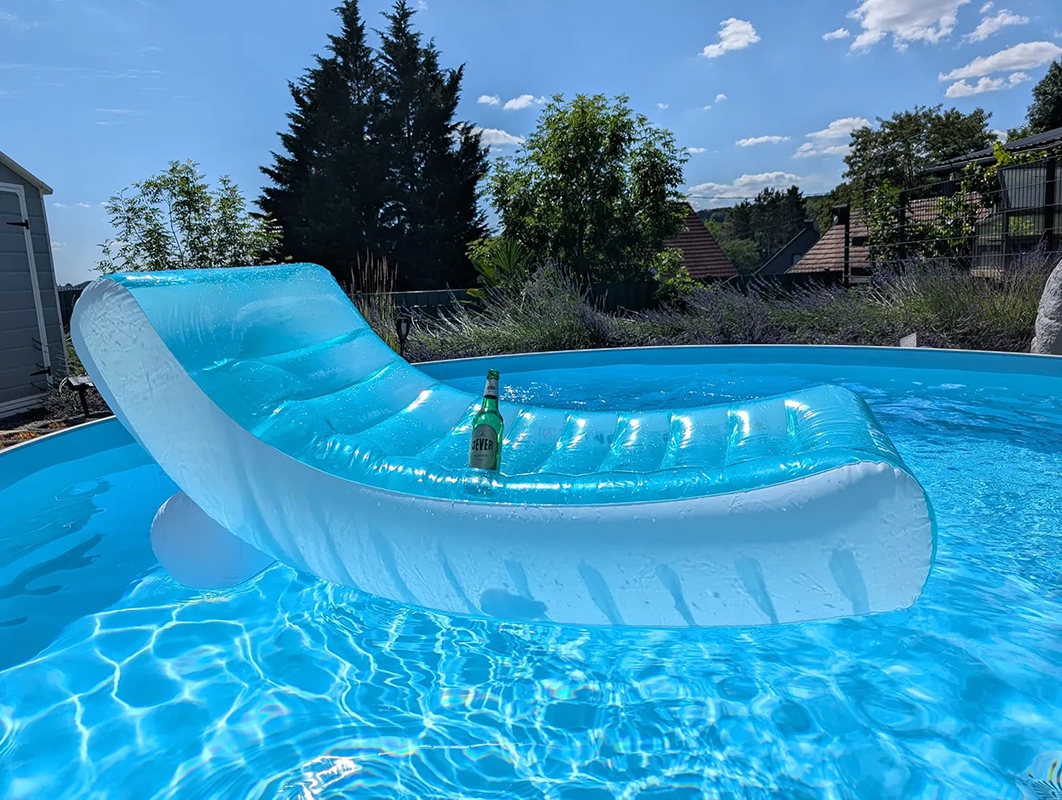 Aufblasbare Liege mit einer Jever Flasche in einem runden Pool. Im Hintergrund Bäume und Häuser unter blauem Himmel.