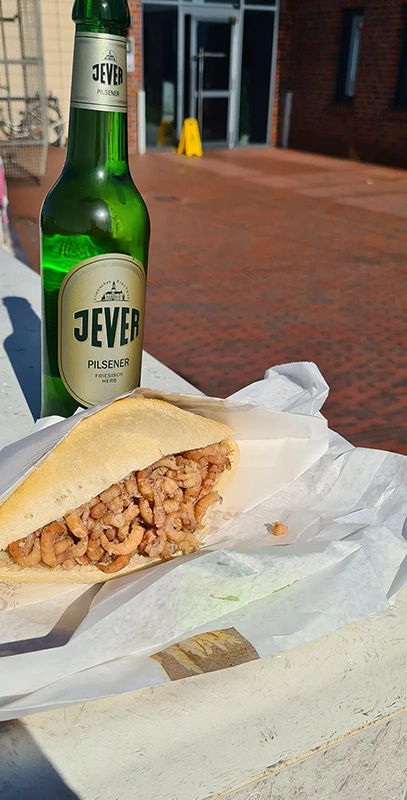 Ein Brötchen mit Krabbenfüllung liegt neben einer Flasche Jever Pilsener.