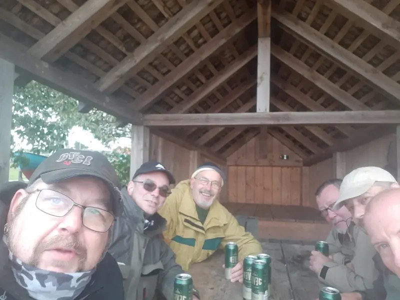 Sechs Männer sitzen an einem Holztisch mit Jever Pilsener Dosen in einer offenen Holzschutzhütte.
