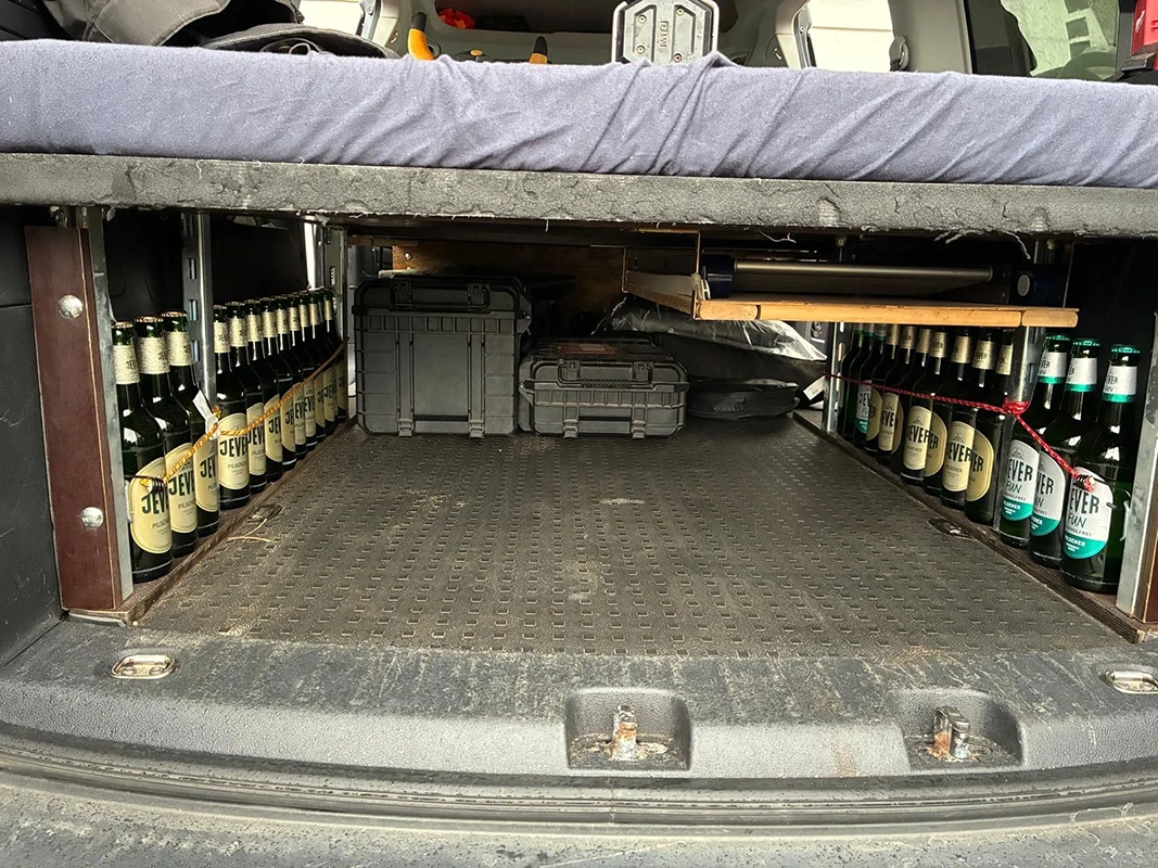 Mehrere Jever Flaschen stehen ordentlich sortiert links und rechts neben Transportboxen unter einem Hochbett im Auto.