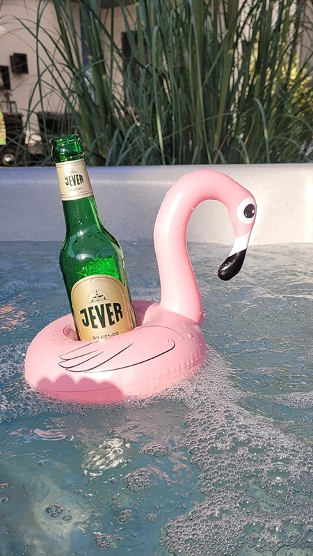 Eine grüne Jever Bierflasche steht in einem pinkfarbenen Flamingo Schwimmring im Wasser. Im Hintergrund Pflanzen.